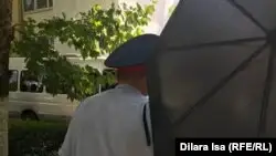 Белгісіз біреу Азаттық тілшісі Динара Исаның камерасын қолшатырмен жауып тұр. Шымкент, 10 маусым 2019 жыл.